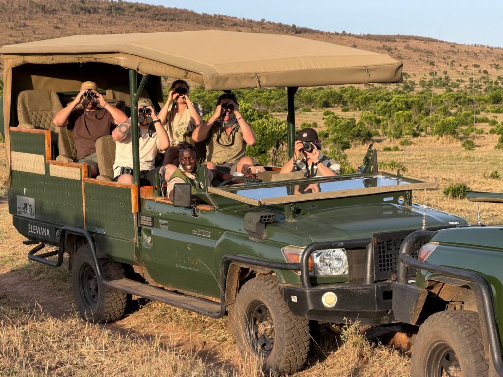 Civilized Adventures guests scanning the plains with binoculars from an open safari vehicle on a game drive in Kenya